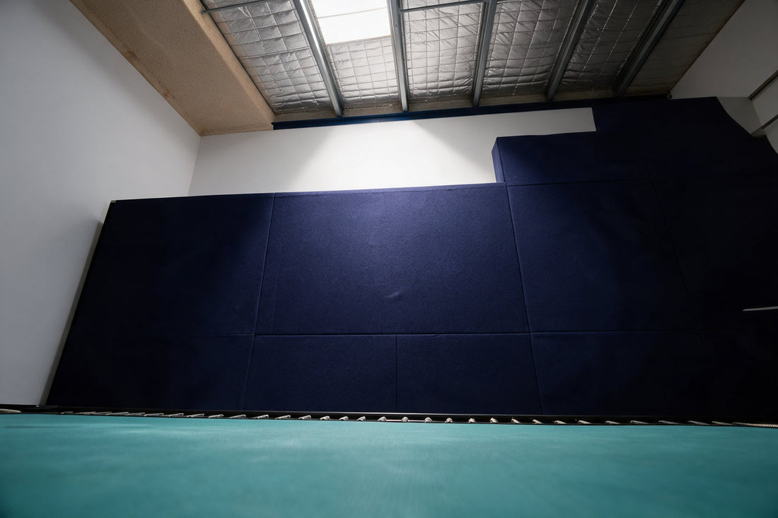 The navy padded wall at Run The Wall seen from the teal trampoline bed, empty, with the skylight above